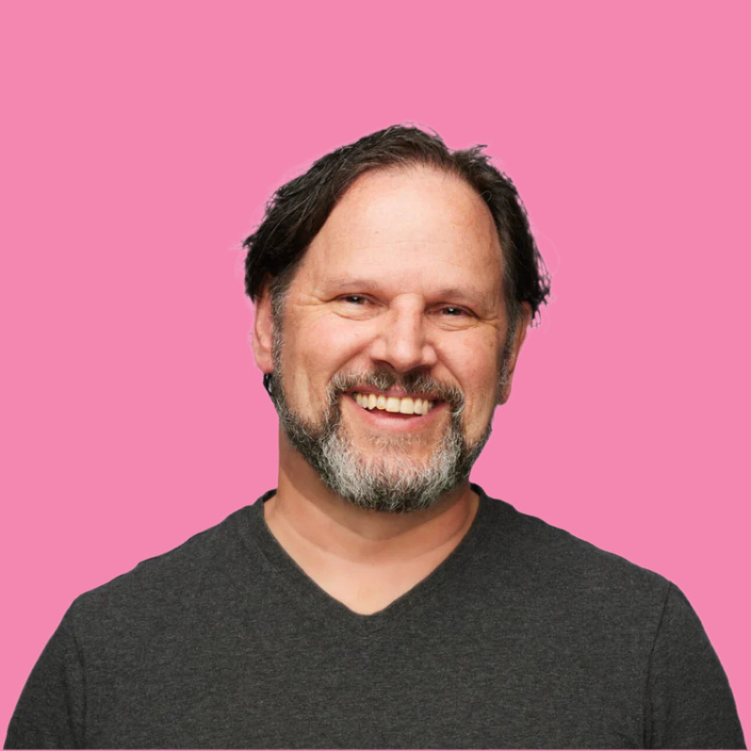 Man with a beard and gray hair wearing a dark gray shirt on a white background. Peter Benes.