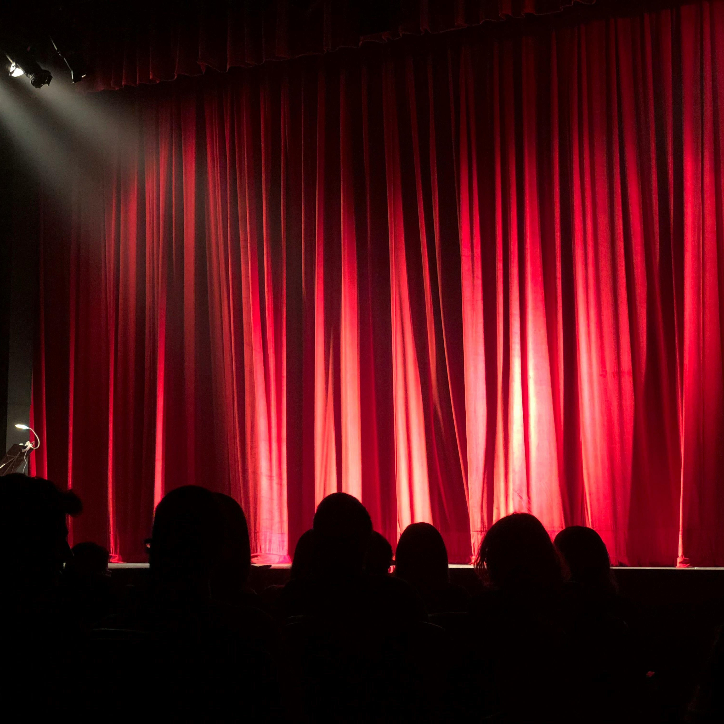 Red theater curtain with silhouettes of audience members and stage lights.